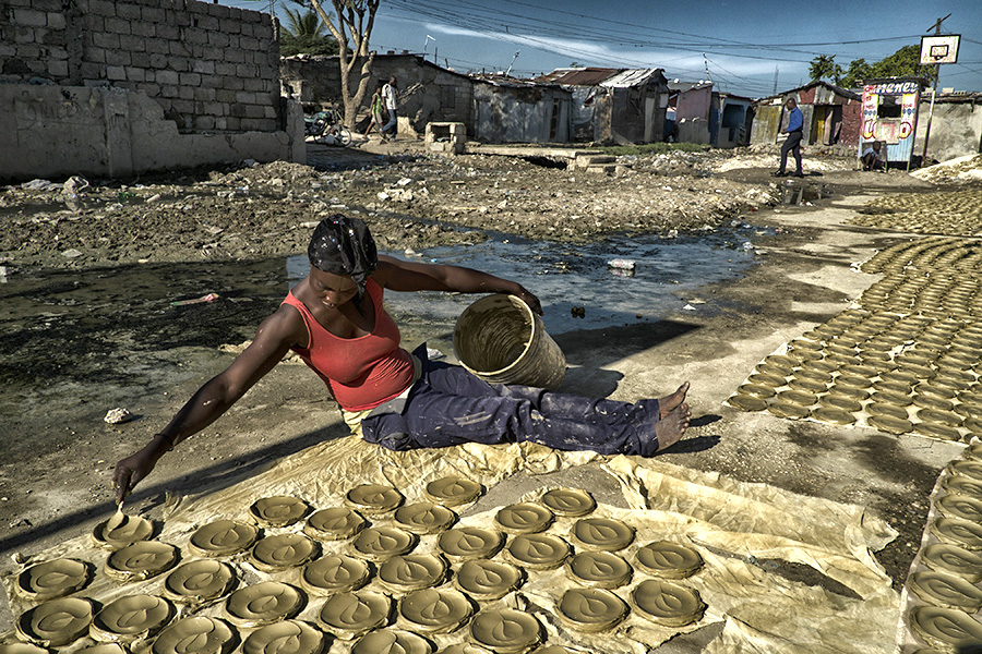 A woman sitting on the ground shapes discs to bake under the sun.