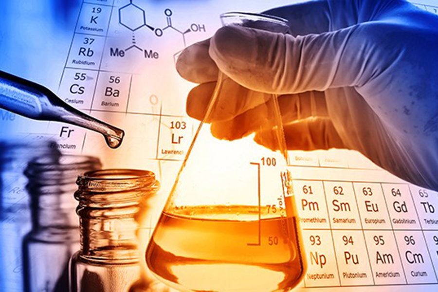 A hand holds a beaker against a periodic chart of elements. 