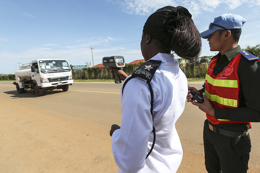 A woman in uniform directs a speed gun at a van while a man in uniform stands behind her. 