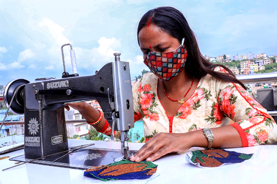 Woman wearing a facemask works on a sewing machine from a rooftop. 