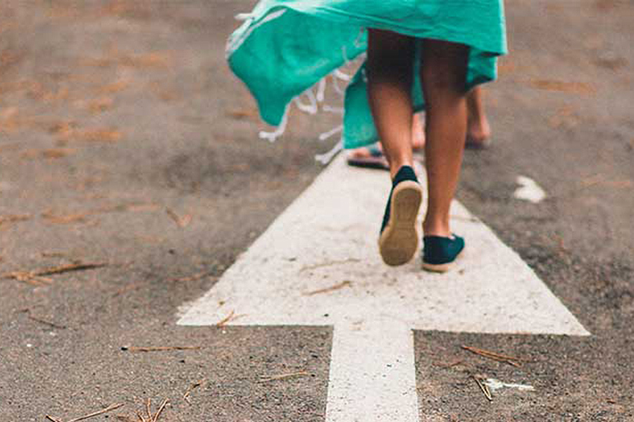 Legs walking away from camera in same direction of arrow painted on the floor. 