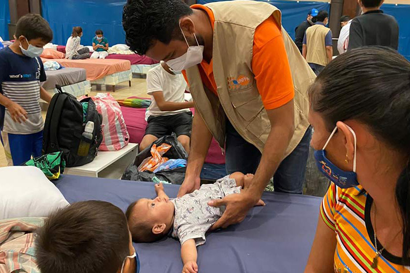 UNFPA aid worker helping a mother with children at a shelter