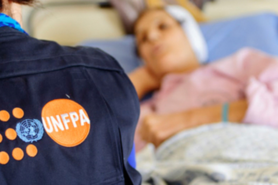 Someone wearing a UNFPA vest sits at the bedside of a patient. 