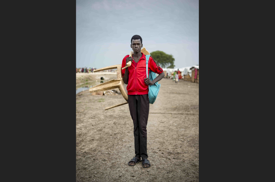 Peter Hoth Tap, a class 4 student aged 16 years, stands with the chair he carries to school each day.