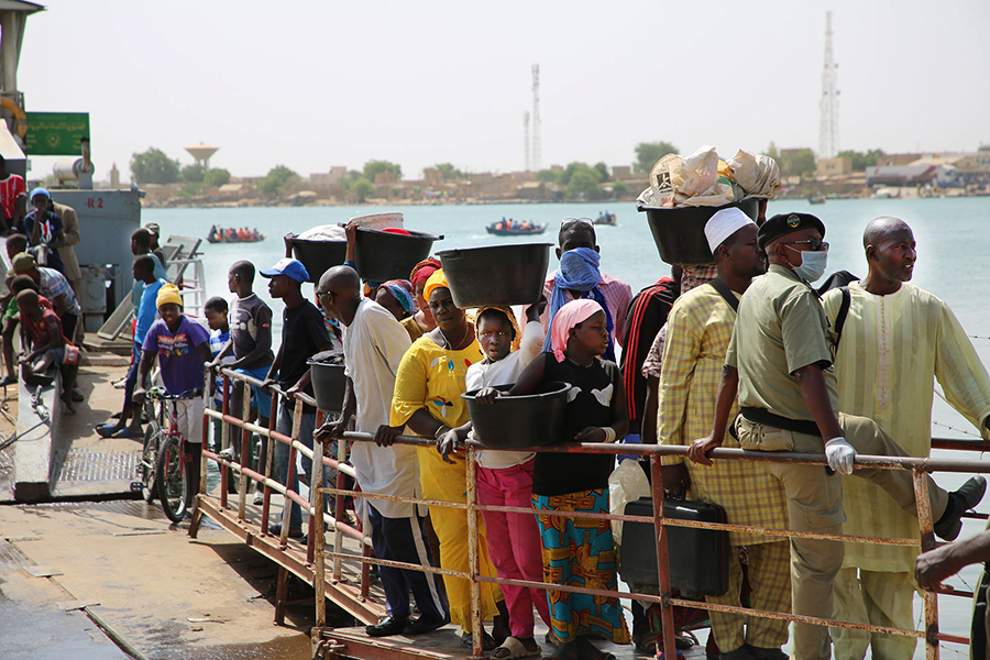 People, carrying their belongings, line up at a port.