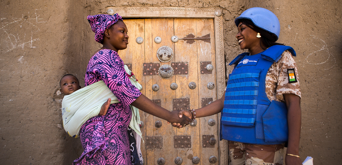 a woman in blue helmet shakes hands with a woman carrying a baby on her back