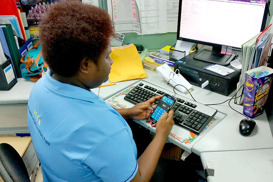 A person sits in front on their computer staring at a mobile phone. 