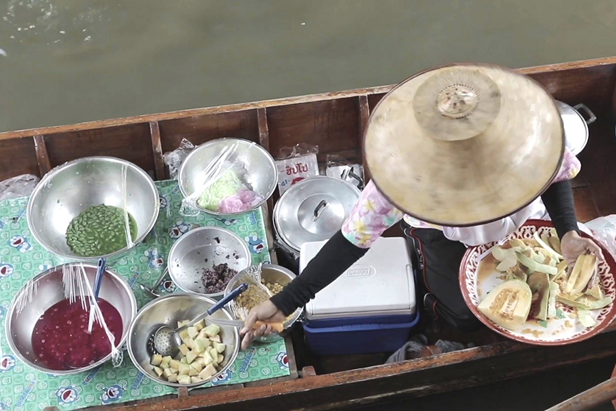 A top-down view of a woman on a rustic rowboat serving food. 