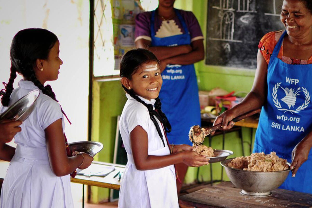 A smiling girl gets served a plate a food by a worker with a WFP apron in Sri Lanka. 