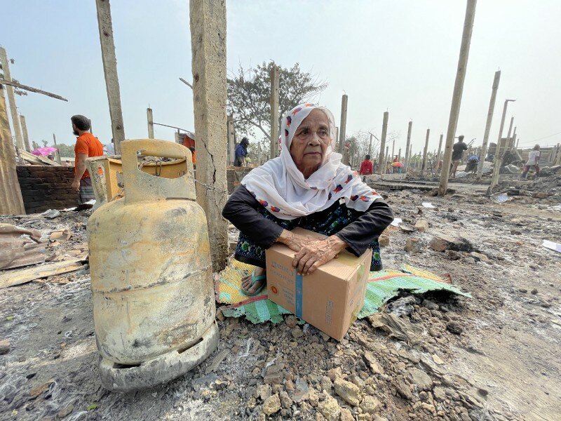 elderly woman sits in ruins with box of food