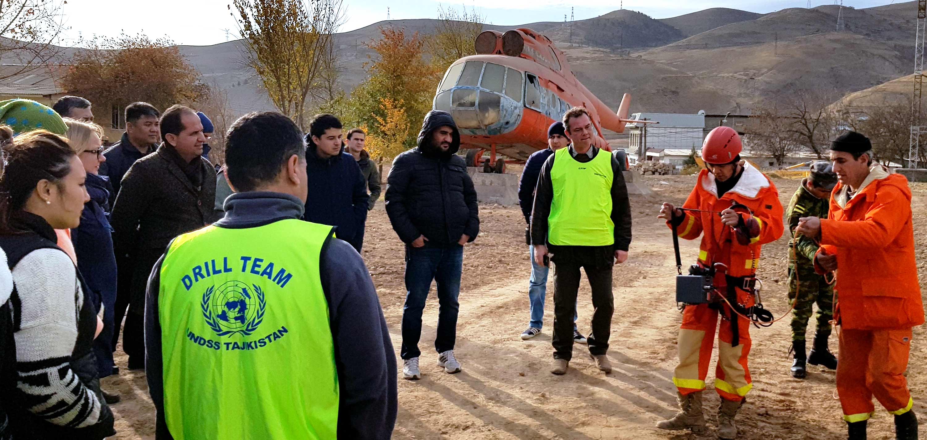 Men and women receive training in an open field with a helicopter behind them