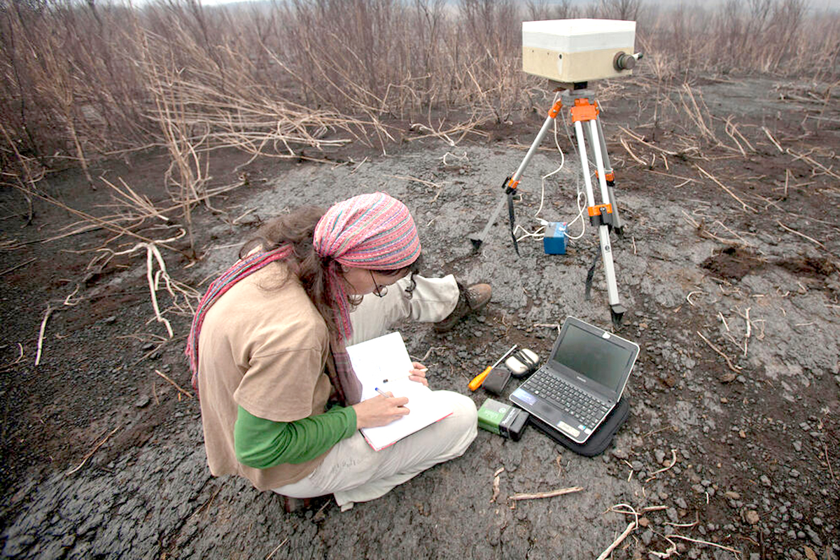 A woman inside a volcano crater with monitoring equipment.