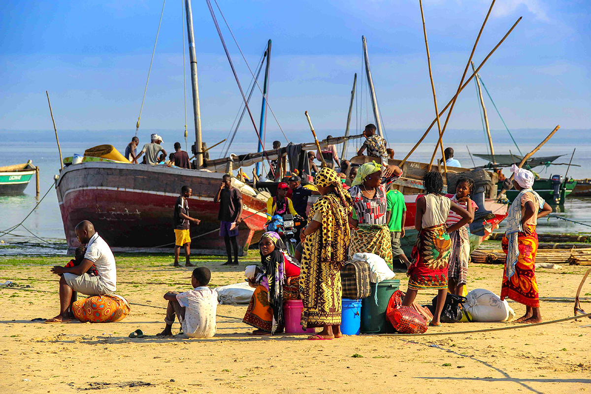 People gathered on the beach with bags in front of a boat.