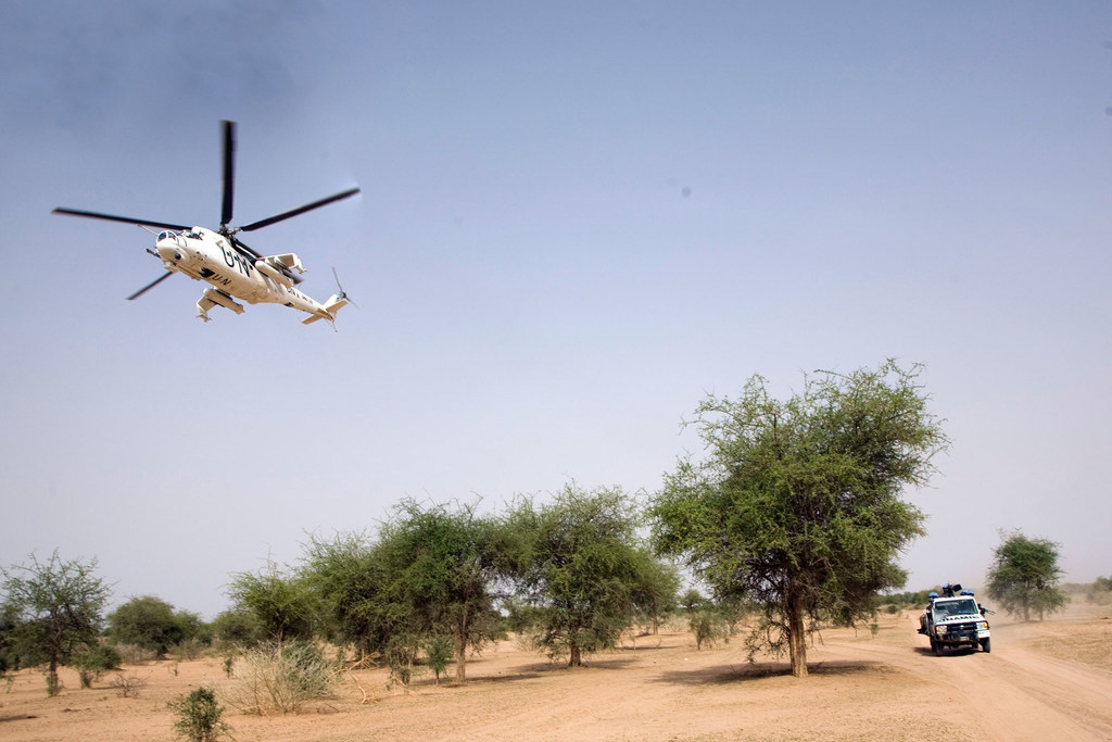 A UN-marked helicopter flies above a truck that reads UNAMID.