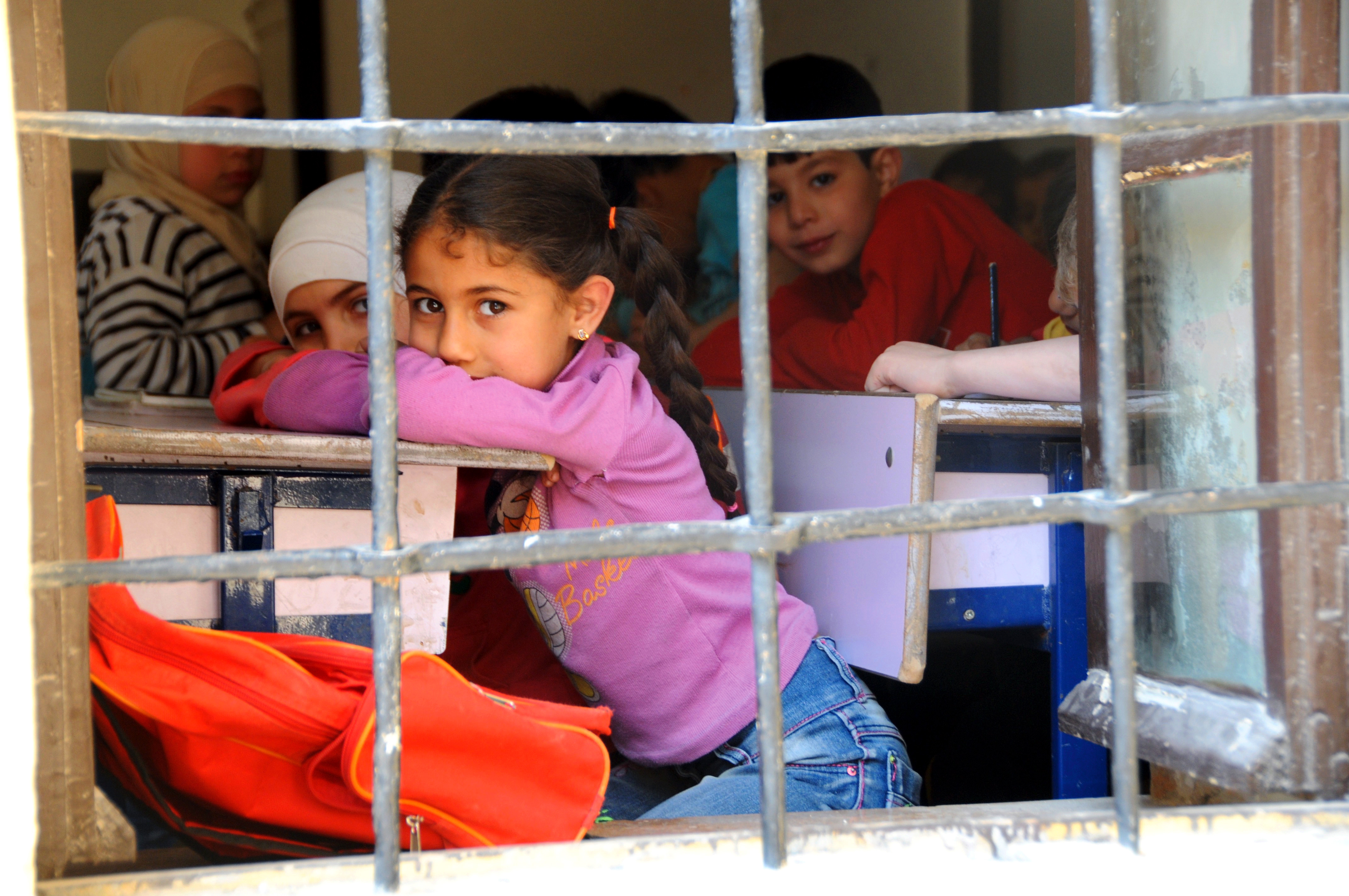 A girl looks out a window with bars from inside the classroom. 