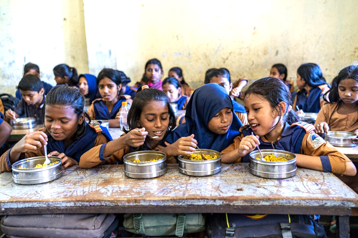 4 girls eating lunches from a metal lunchbox sitting at the same side of a desk. 