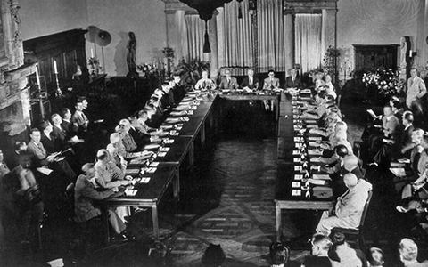 >Dozens of Representatives of the Soviet Union, the United Kingdom and the United States meeting in a large room with two tables across from each other in 1944.