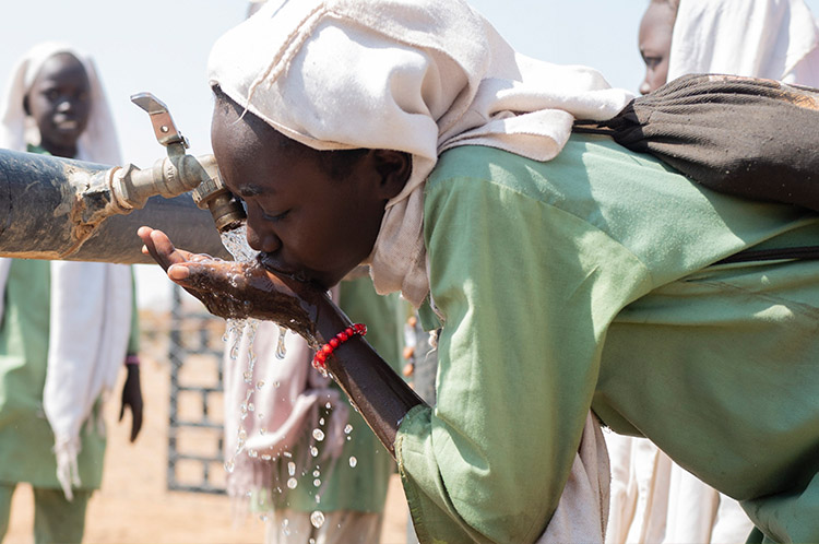 Une jeune fille boit de l'eau à un robinet en plein air.