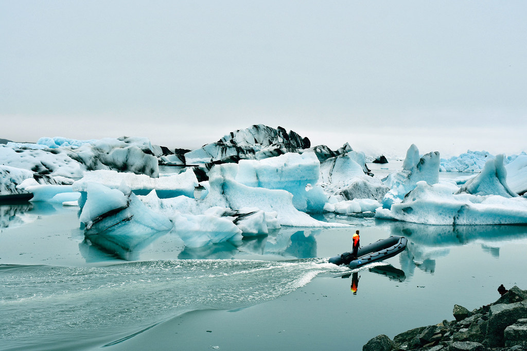 Boat in a lagoon with big blocks of ice crumble from a shrinking glacier