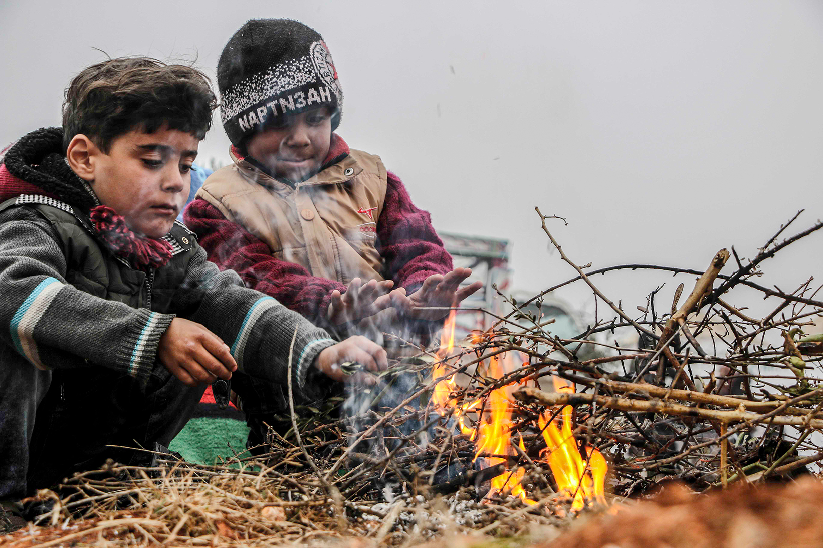 young Syrian children warming themselves over a fire
