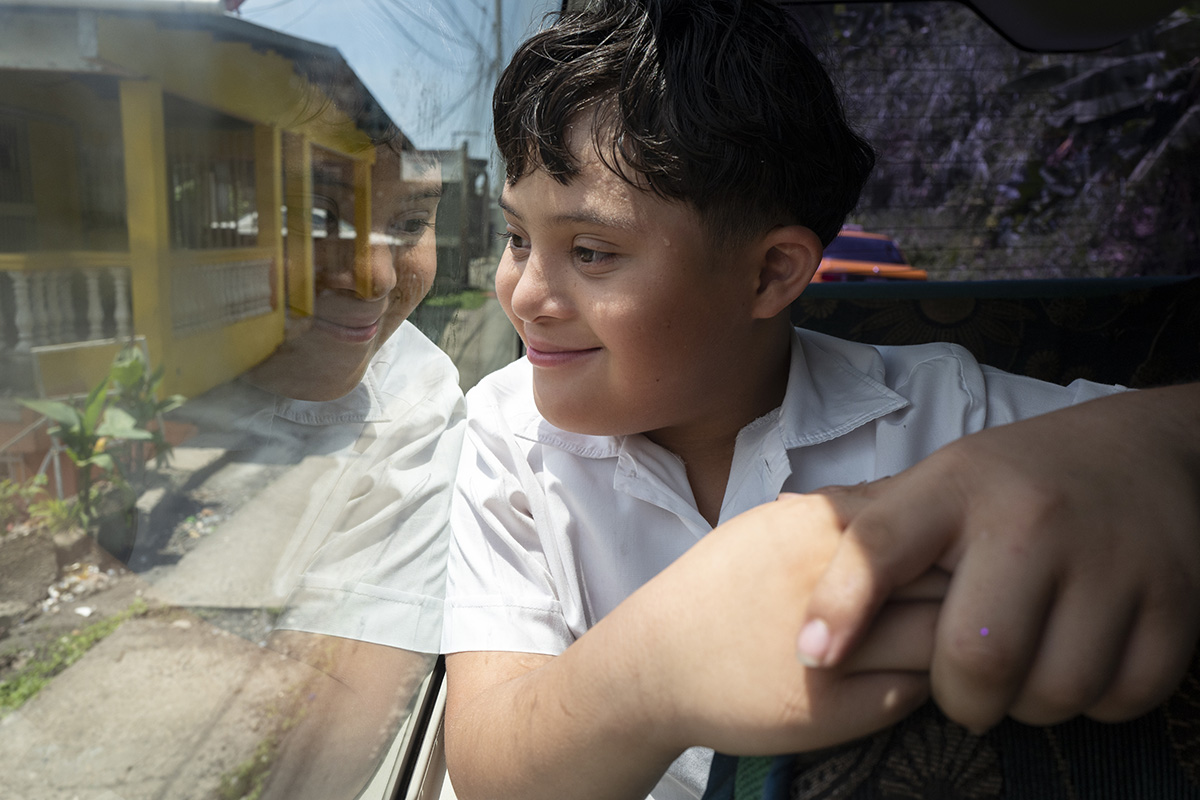 A boy with Down syndrome looks out the window of a bus.