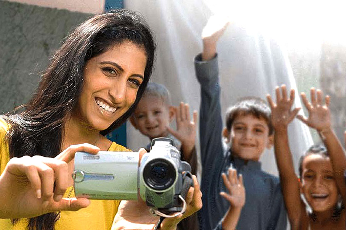 A woman holds a video camera while kids hold up their arms. 
