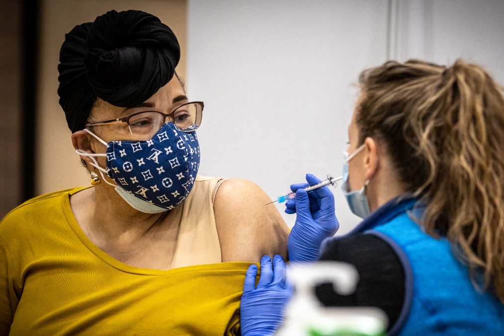 Woman wearing a facemask pulls down her sleeve to get the vaccine. 