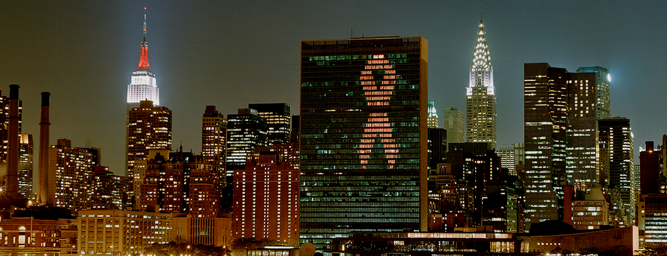El edificio de la Secretaría de las Naciones Unidas está iluminado con la cinta roja del SIDA por la noche, como se ve desde el East River en la ciudad de Nueva York.