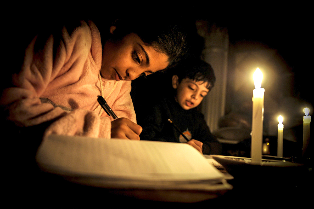 A girl and a boy study under candlelight.