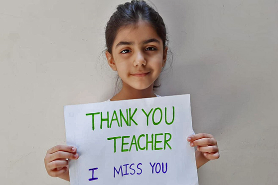 Una niña de Pakistán con un cartel que dice "Gracias maestra, te extraño"