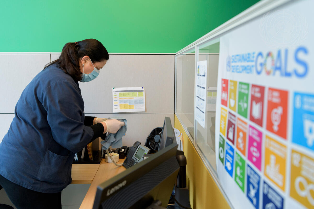 A woman wearing a face mask wipes a phone at an office desk.