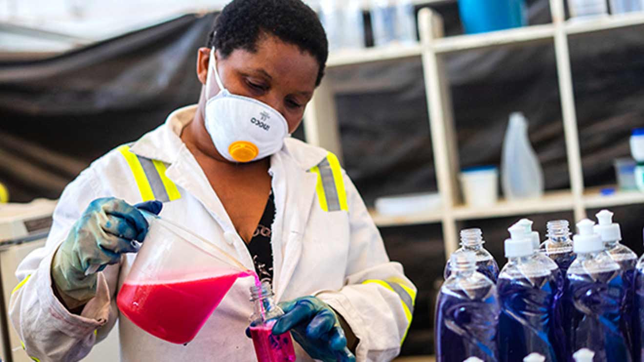 Woman wearing a mask pours a liquid into a container. 