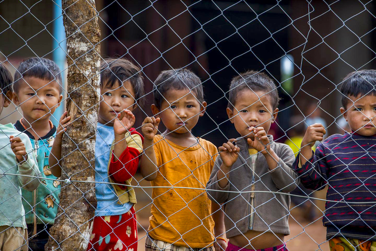 5 boys look out from behind a fence.