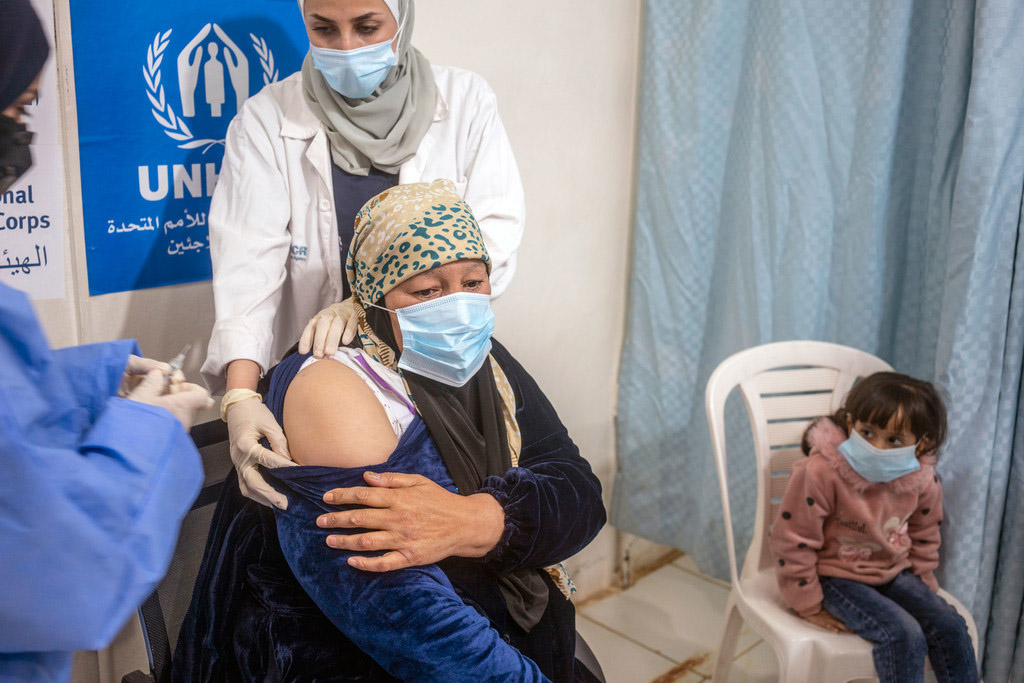 Older woman getting vaccinated, while a little girl watches.