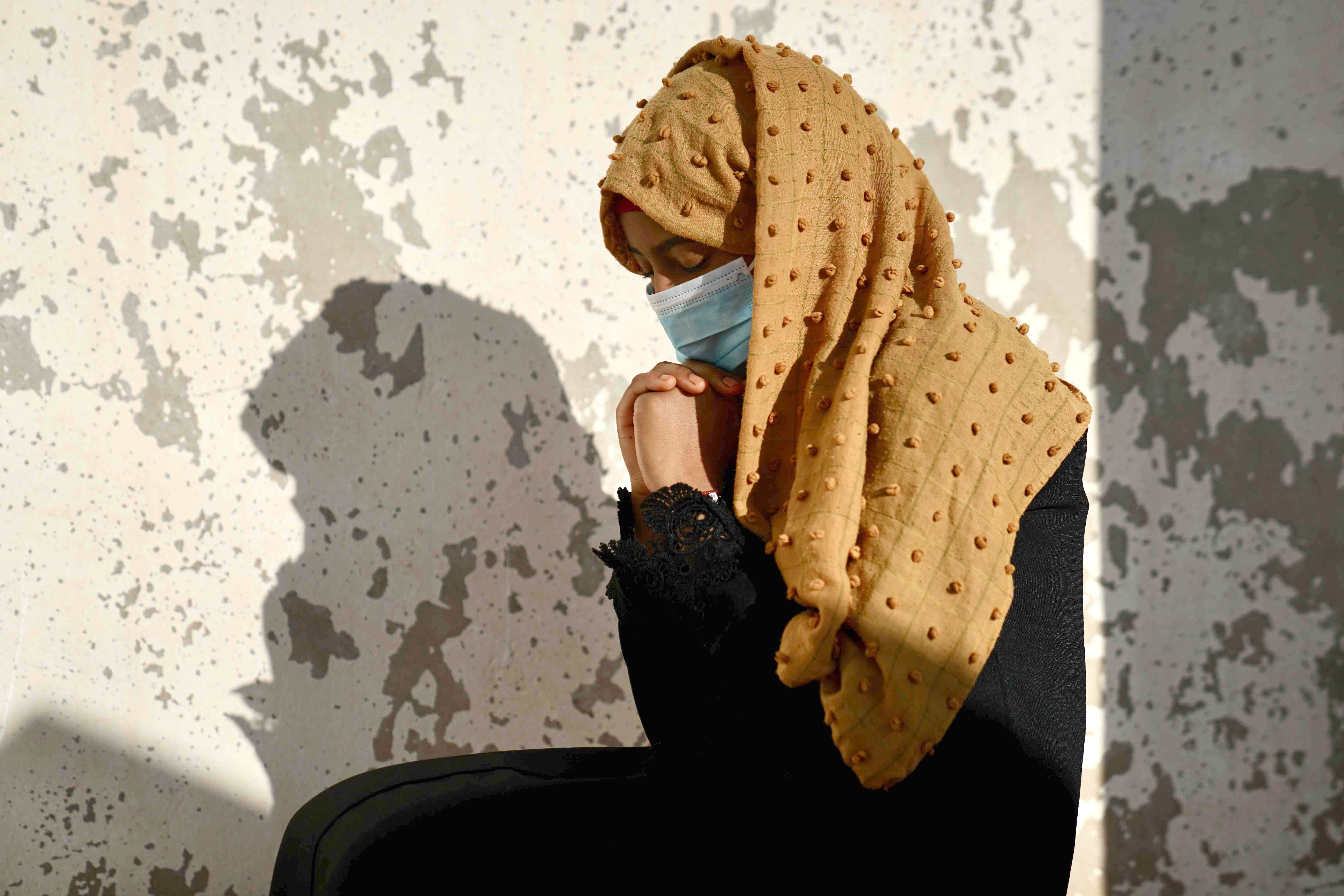 A woman with eyes closed looks down and leans her head on her hands in prayer position.