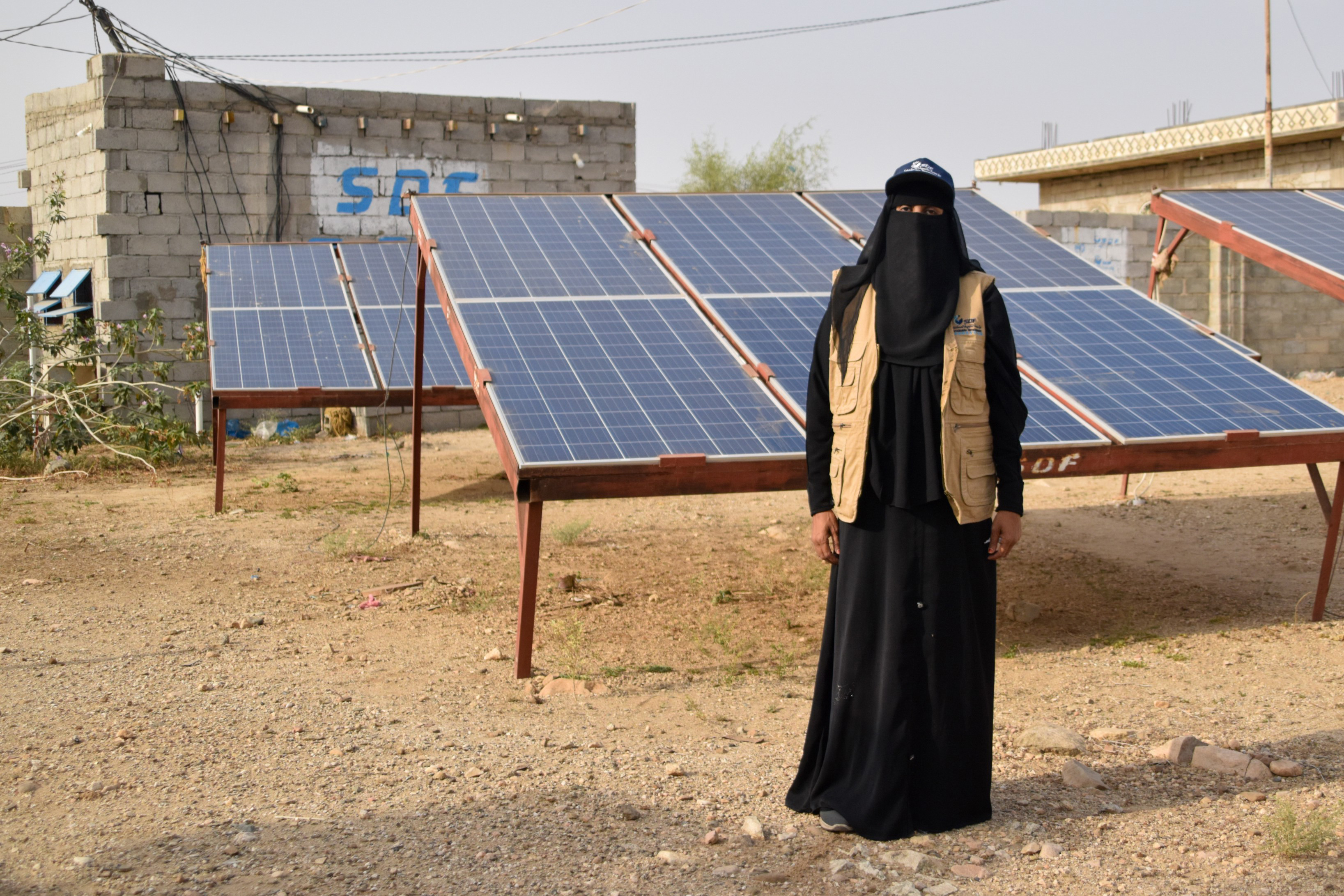 Iman Hadi poses for a picture next to rows of solar panels.