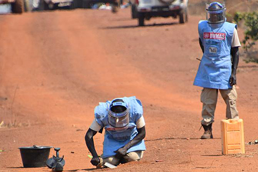 Two UN Mine Action Service staff demine a road.
