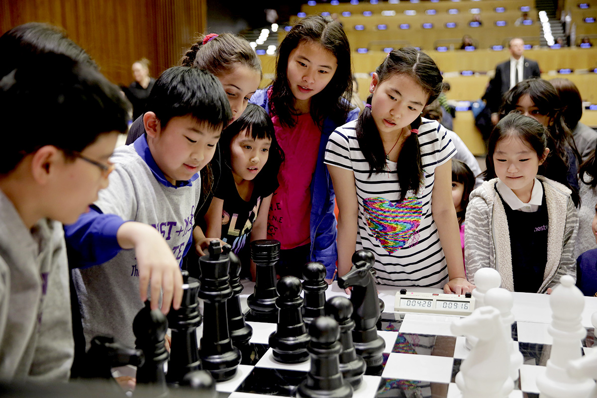 a group of children surround a big chess board looking for the next play