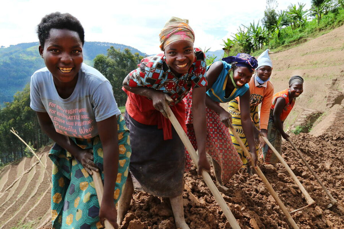 a group of women using hoes to till the soil