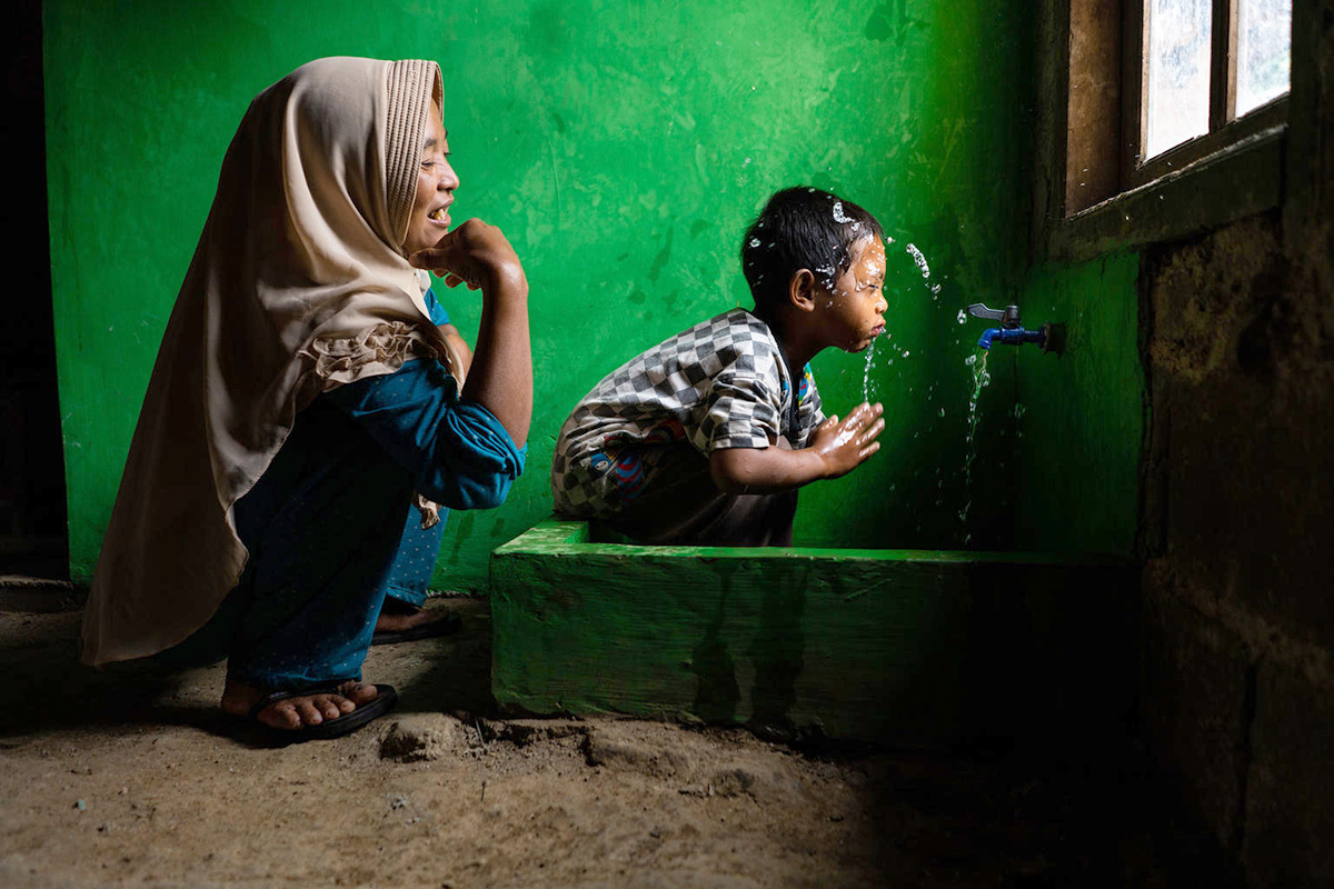 a woman squats next to a boy splashing water