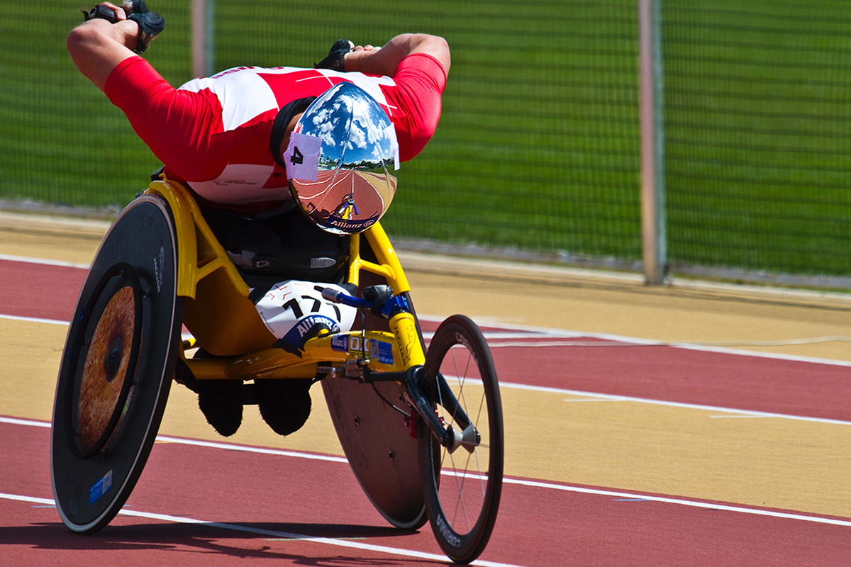 Man in red jacket and helmet riding a yellow wheelchair.