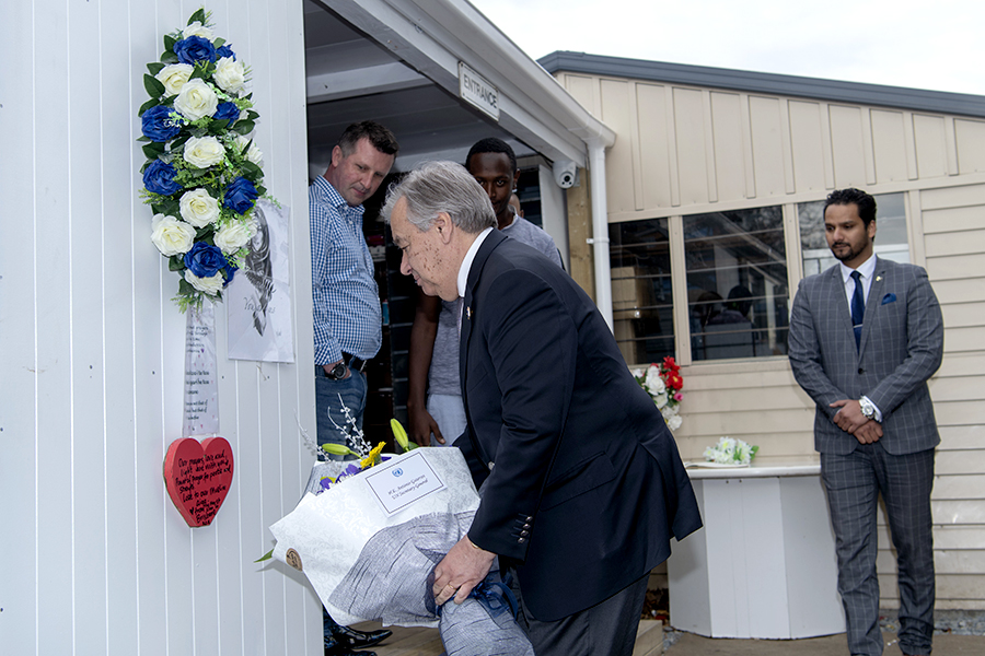 Man bows and lays flowers by a wreath of flowers.