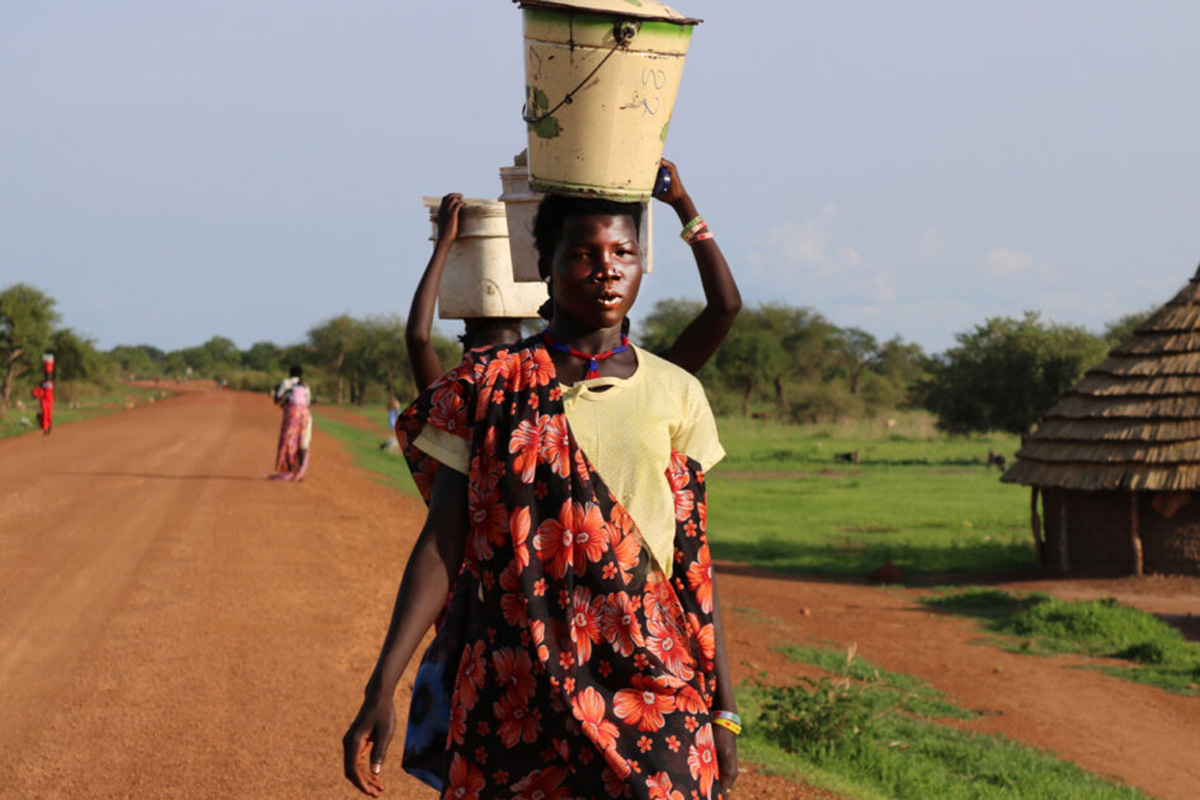 Women walking along a road carrying buckets on their heads.