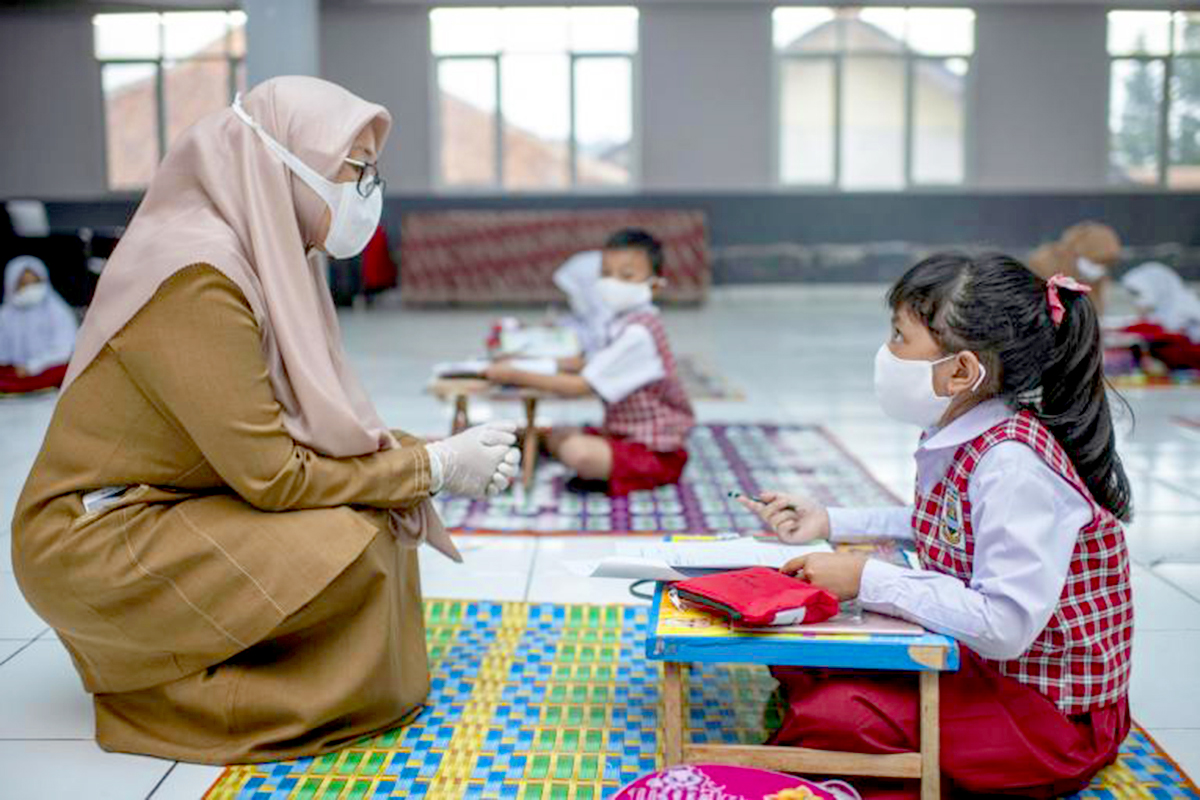  A teacher squats in front of a student sitting on the floor in front of a short desk. 