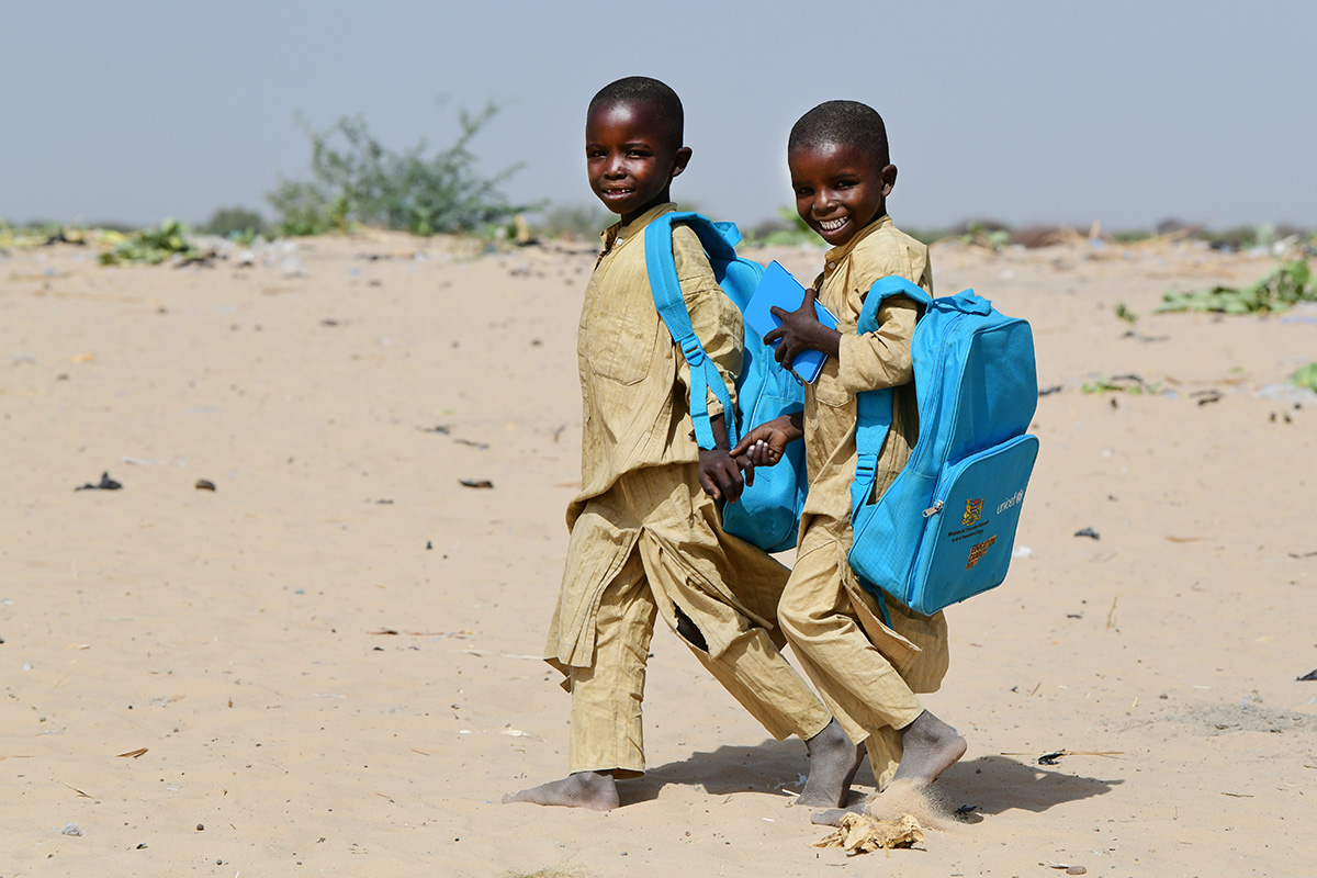 Two smiling children walk in the desert carrying UNICEF backpacks 
