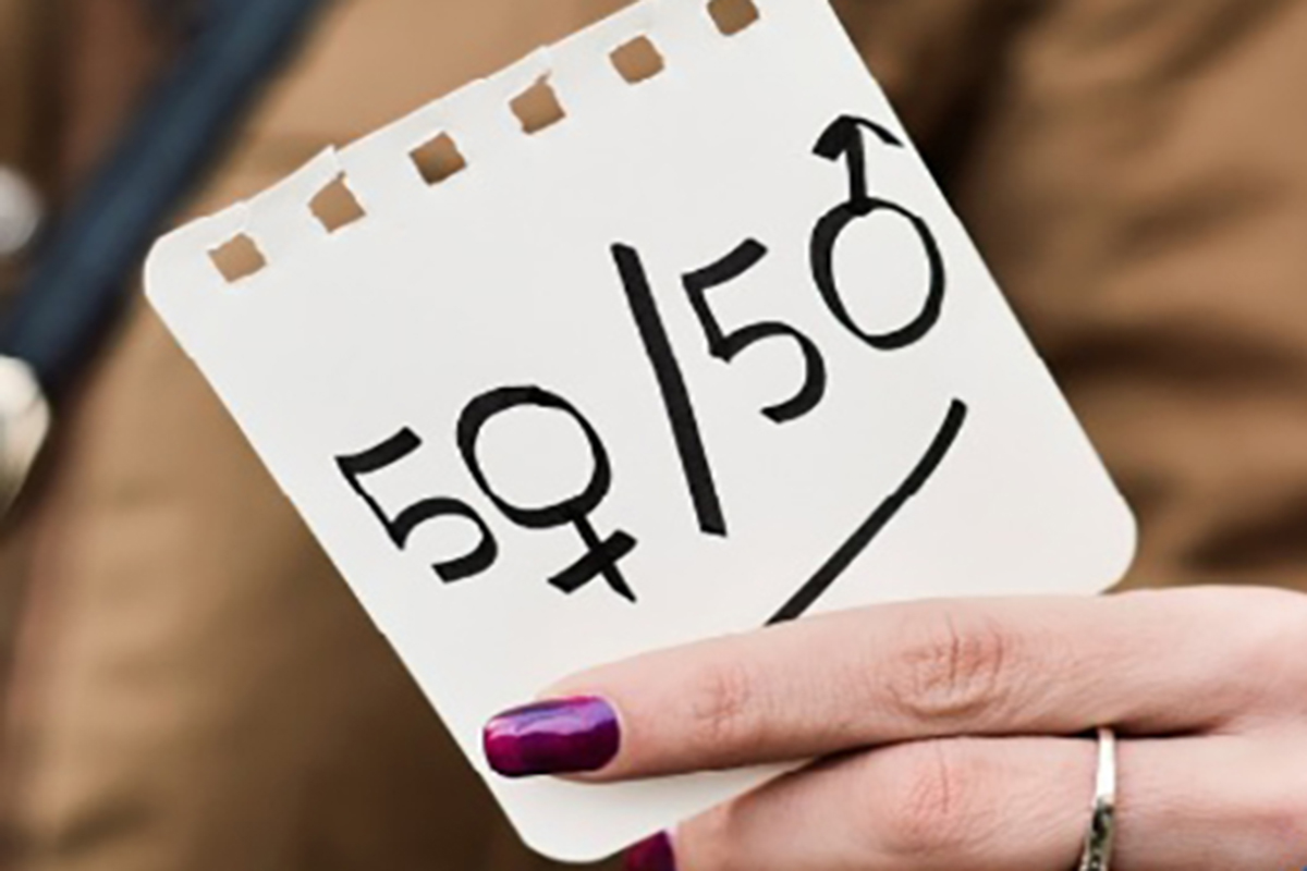 A woman hangs holds up an illustration of a 50/50 signs that include both the male and female signs.