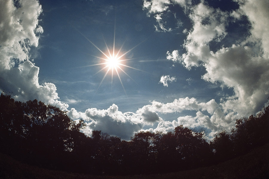 The bright sun in a blue sky surrounded by clouds.