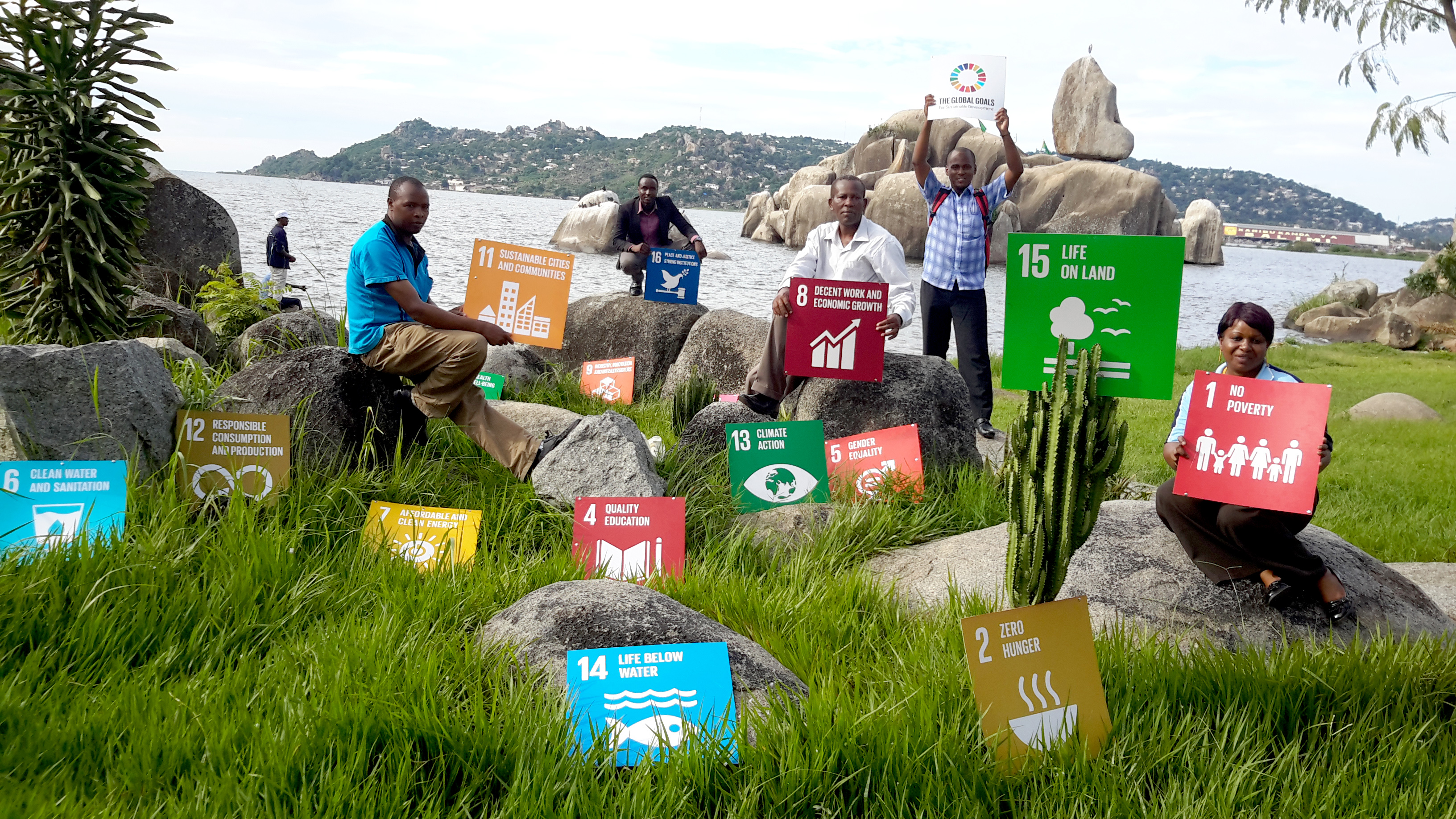 People sitting outdoors close to a lake holding up SDG signs