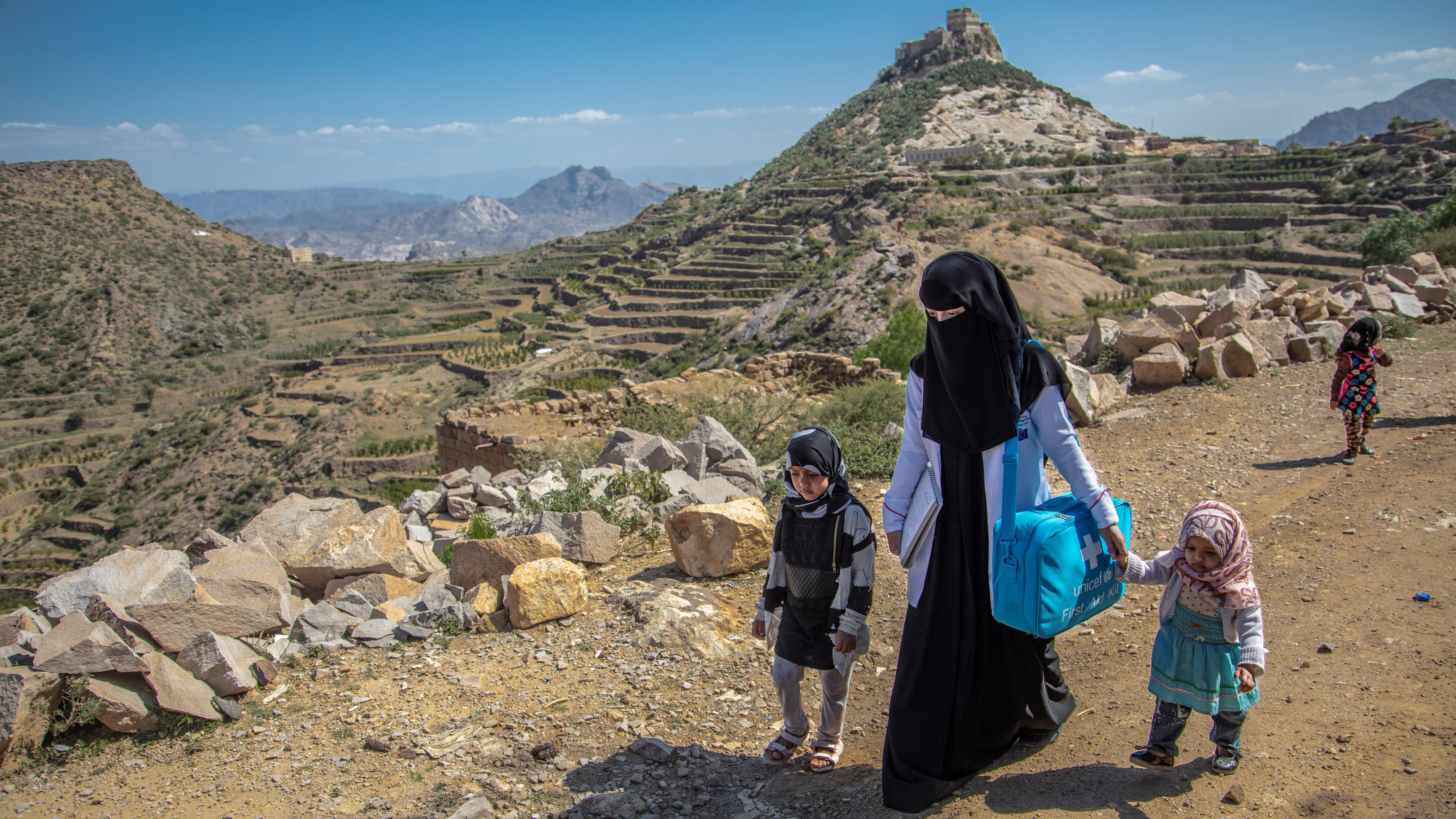 Une femme portant un voile islamique marche avec deux enfants sur un territoire montagneux aride.