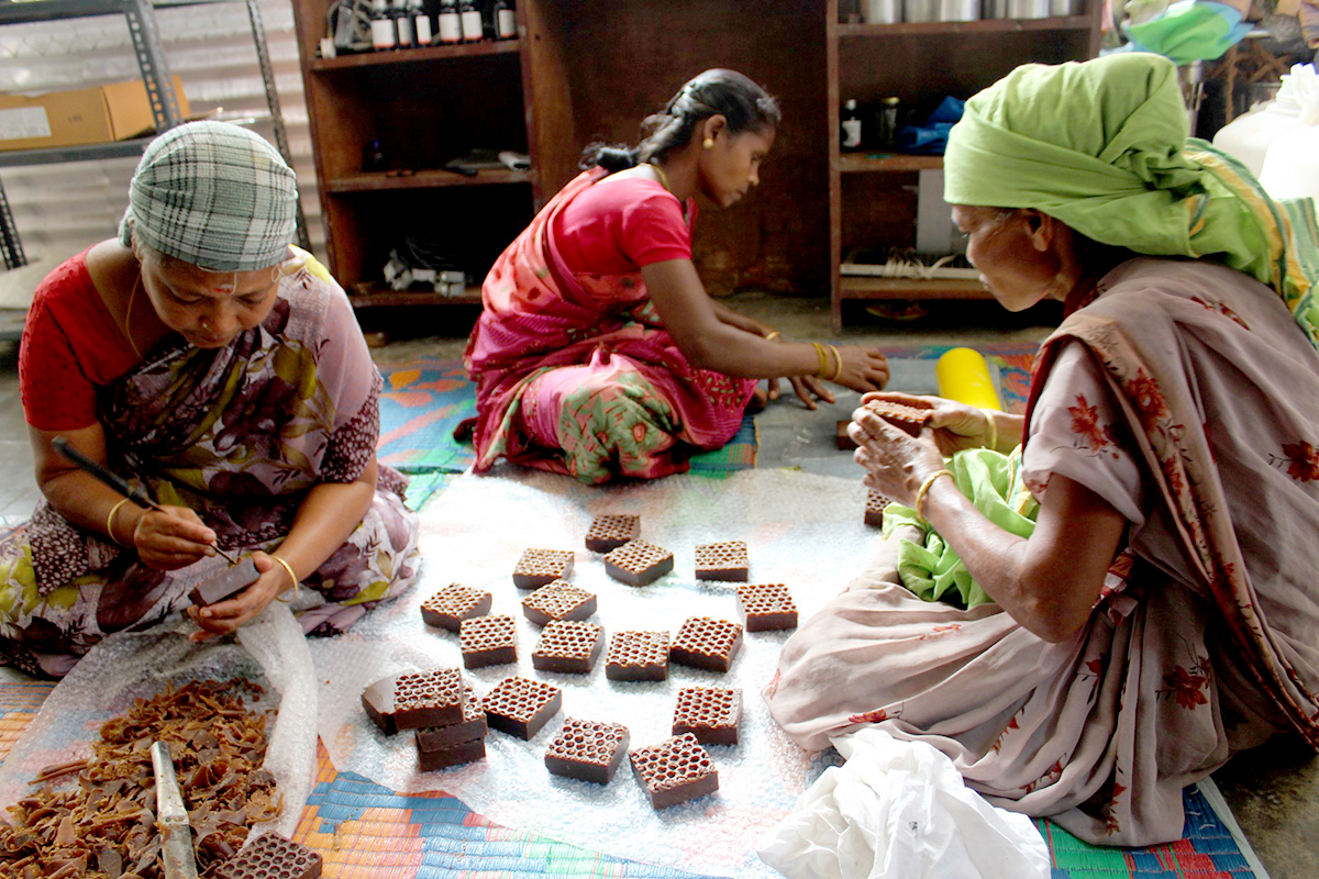 Women sit on the ground removing wax from honeycombs. 